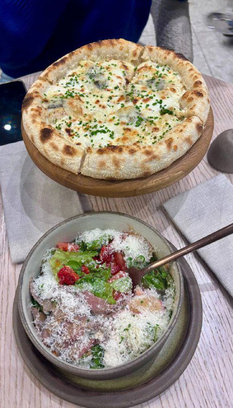 Фото еды: тонкая пицца с зеленью и миска с салатом/гарниром, сервировка на столе в одном из итальянских ресторанов, вид с ракурса клиента.