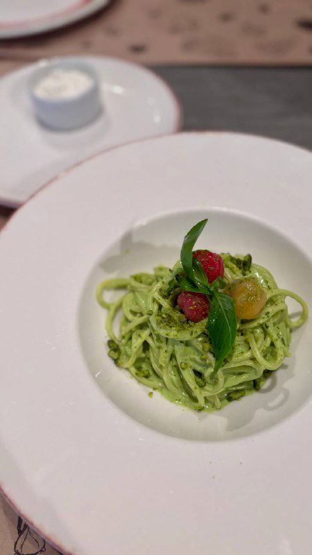 Крупный план зелёной пасты с томатами и зеленью, сервированная в глубокой тарелке — пример блюда, которое автор пробовал в ресторане.