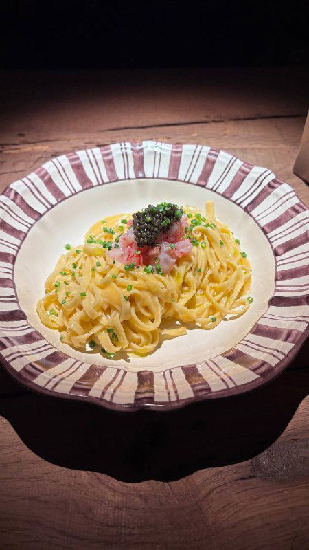 Тарелка пасты в ресторане «За Крышей»: кремовая паста с икрой и зеленью на декоративной тарелке, снята при тёплом боковом свете.