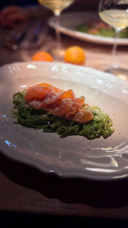 Холодная закуска: ломтики лосося на зелёной подложке (паста или салат), акцент на свежести и контрасте цветов на белой тарелке.