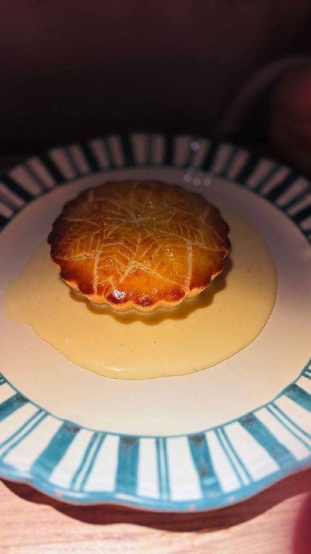 Запечённый десерт с золотистой корочкой на тарелке, подан на столе с соусом — крупный план демонстрирует текстуру и цвет.