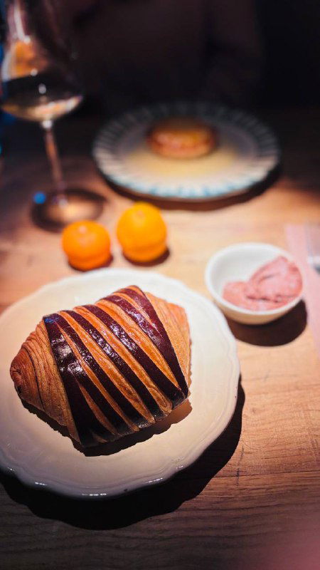 Слойка с шоколадной полосатой глазурью рядом с порцией мороженого — элегантная подача и бокал вина в глубине кадра.