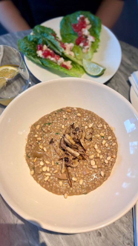 Другая подача блюд в ресторане КМ20: тарелка с кремовым ризотто или похлебкой и листовой зеленью, вид крупным планом.