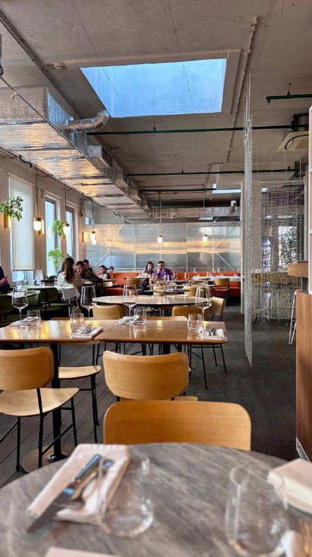 Общий зал ресторана КМ20 с окнами и столами, светлая просторная обстановка и современные деревянные стулья, дневное освещение.