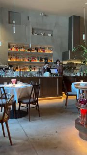 Светлый и просторный интерьер Rebecca: барная зона со стеллажами, столы и стулья, ненавязчивая ресторанная атмосфера и теплый свет.