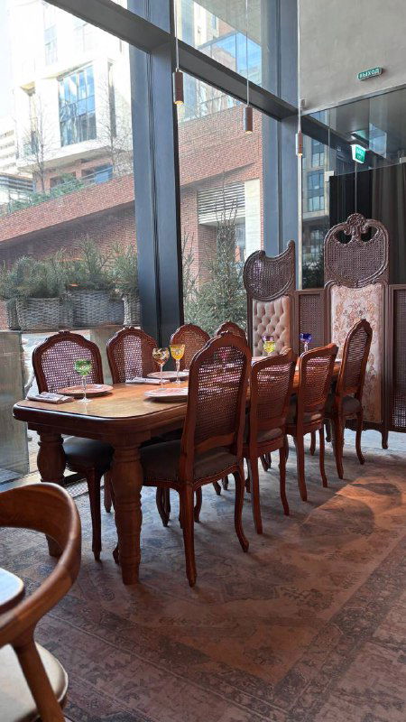 Уютный стол у большого панорамного окна в Rebecca: деревянные стулья, столовая сервировка и вид на внутренний двор комплекса ЖК Садовые кварталы.