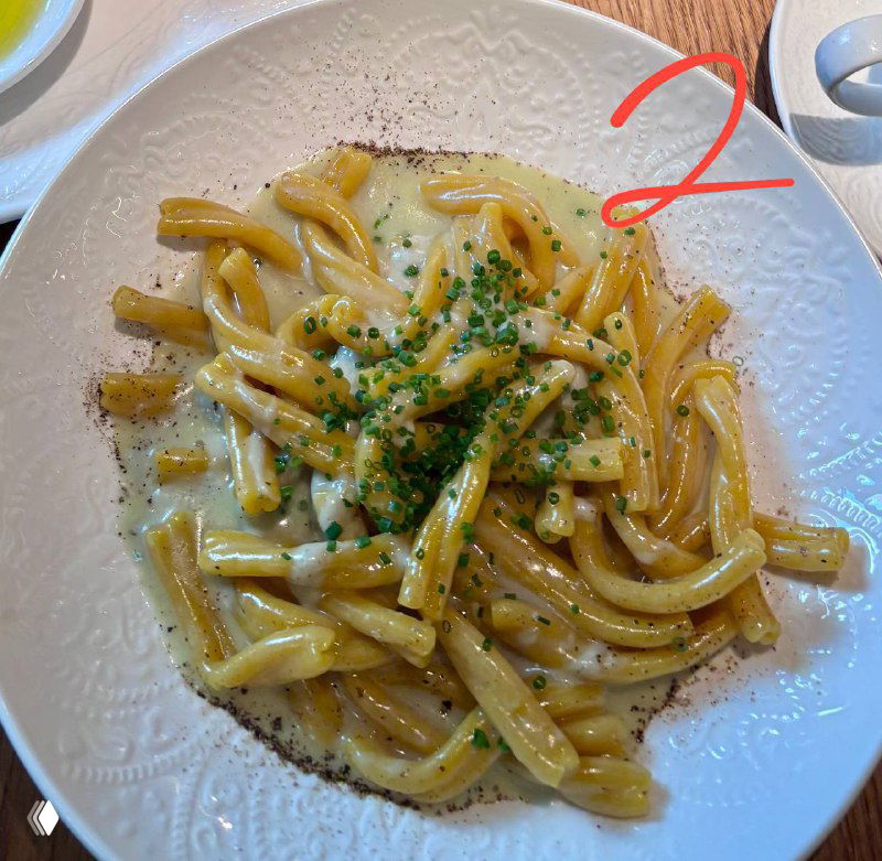 Белая тарелка с кремовой пастой, посыпанной зелёным луком и чёрным перцем; в кадре видна красная цифра «2», крупный план подачи.