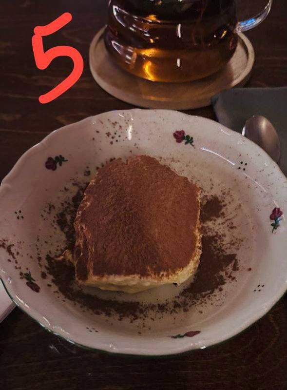 Квадратный кусок тирамису на винтажной тарелке, сверху какао, рядом чай — снимок демонстрирует классический вид десерта.