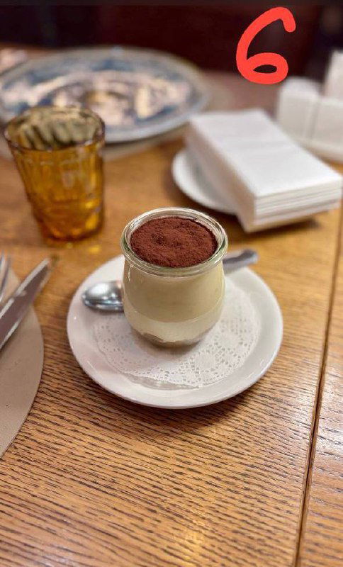 Маленькая порция тирамису в стеклянном стаканчике с ложкой на подставке, аккуратная подача в кафе, кадр обзора.