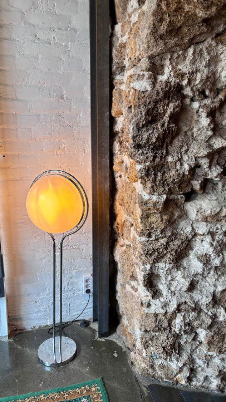 Напольный торшер у фактурной кирпичной стены и грубого каменного участка, создающие контраст текстур в интерьере ресторана.