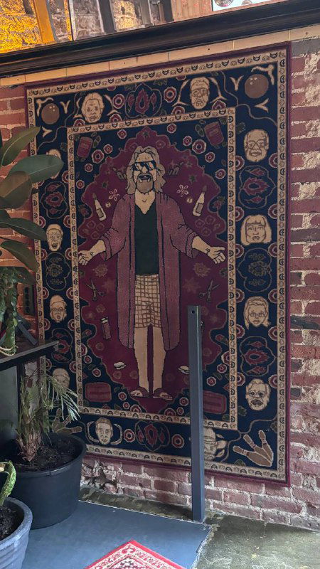 Декоративный настенный ковёр с изображением персонажа в центре, висящий на кирпичной стене — акцентный элемент в оформлении заведения.