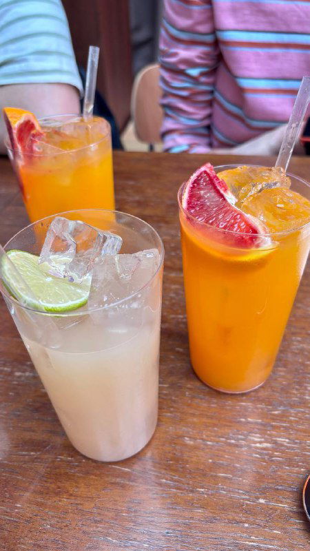 Несколько холодных напитков в стаканах разной формы на столе: яркие соки и лимонады в неформальной подаче в ресторане.