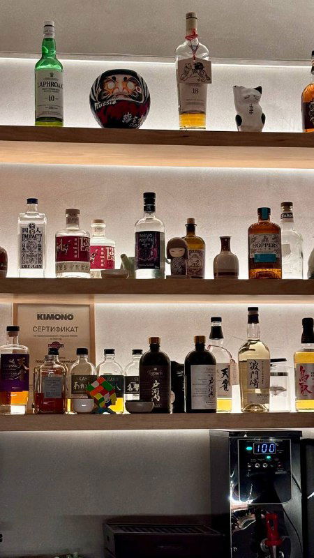 Подсвеченные полки с разнообразными алкогольными бутылками: сочетание японских и международных напитков в баре.