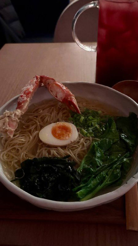 Большая миска рамена с крабом, половинкой яйца, ошпаренным шпинатом и водорослями вакаме на фоне деревянного стола.