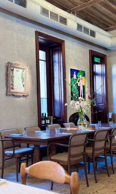 Другая панорамная зона зала Mamie: длинный стол, современная художественная картина на стене и букет цветов на столе, вид крупным планом.