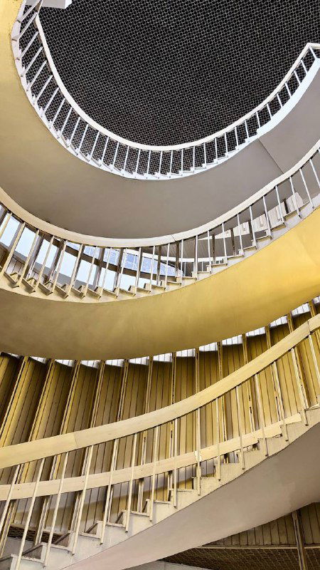 Взгляд снизу вверх по двойной спиральной лестнице: пересекающиеся дуги и геометрические формы, создающие ощущение витка и глубины в библиотеке.