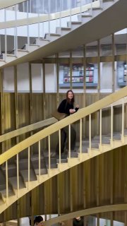 Женщина поднимается по одной из лестниц библиотеки, видно перекрытие балюстрад и информационные таблички на стенах в глубине кадра.