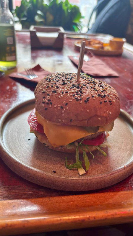 Сочный веганский чизбургер на тарелке: булочка с семенами, растительный сыр, лист салата и сочные ингредиенты крупным планом.