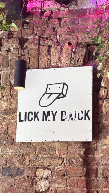 Белая табличка с провокационной надписью на кирпичной стене внутри кафе Mission — элемент уличного хипстерского декора интерьера.