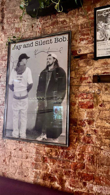 Чёрно-белый постер Jay and Silent Bob на кирпичной стене кафе Mission — винтажный постер среди другого декора и плакатов.