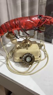 Крупный план телефон-лобстера — арт-объект Дали с красной панцирной формой и винтажным телефоном, экспонат на белой подставке в музее