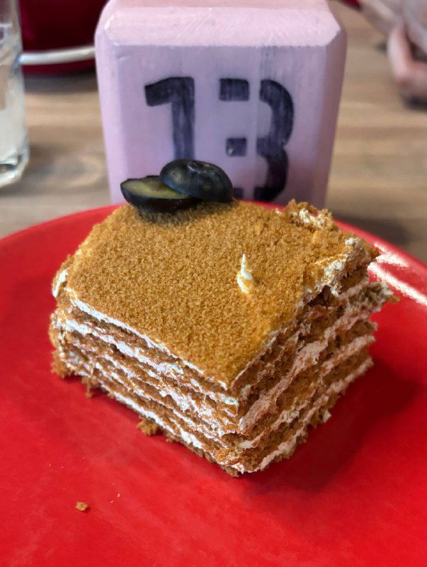 Кусок медовика на красной тарелке: видны слои коржей с кремом и крошка сверху, аккуратно нарезанный десерт в кафе.