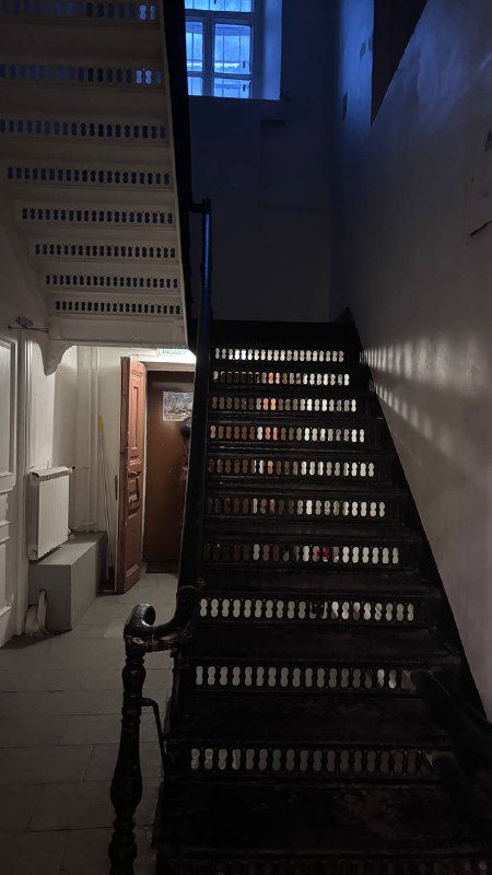 Тёмная деревянная лестница в старом помещении трапезной, вид на верхние витые перила и строгое архитектурное решение внутри здания.