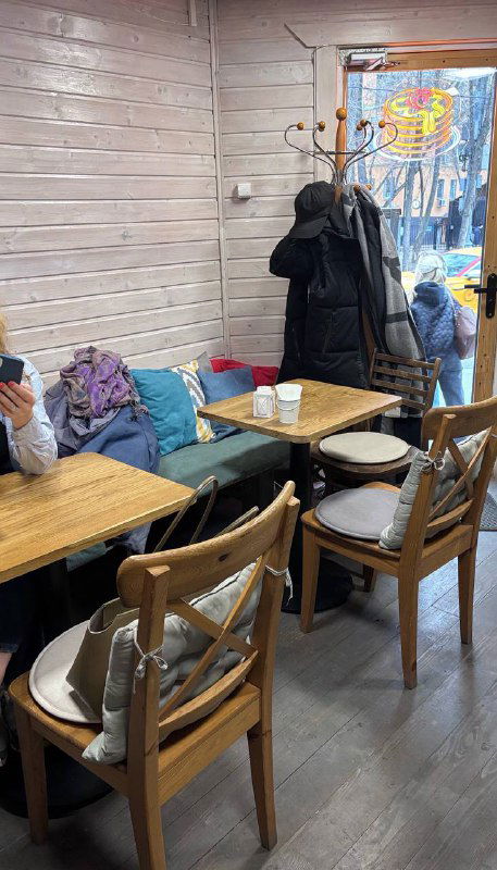 Небольшое внутреннее пространство кофейни с деревянными столиками, стульями и монохромным декором — уютное место для посиделок.