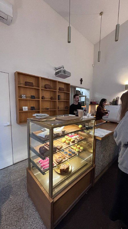 Витрина с кондитерскими изделиями в кофейне при культовом месте — стеклянная прилавочная витрина и барная зона за ней.