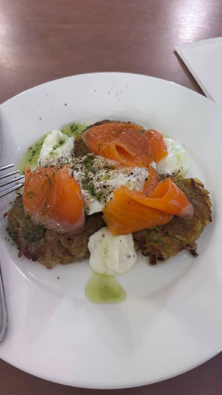 Блюдо из драников с лососем и страчателлой на белой тарелке, крупный план еды в трапезной при храме.