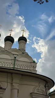 Купола православного храма с крестами на фоне голубого неба и облаков, ракурс снизу показывает бело-зелёную отделку и силуэты куполов.