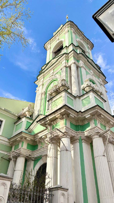 Колокольня с зелёными и белыми элементами фасада: пилястры, карнизы и декоративная отделка, снято при ярком дневном свете весны в Москве.