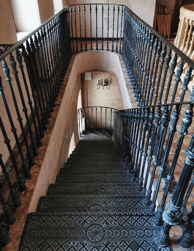 Винтовая чугунная лестница внутри старинного здания при храме: декоративные перила, узорные ступени и историческая фактура интерьера, интерьерный кадр.