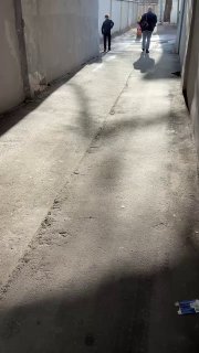 Узкий проход-арка во дворе храма с падающим светом и силуэтами прохожих, тени на бетоне и атмосфера спокойной городской прогулки весной.