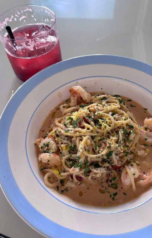 Тарелка с тальолини и креветками в биск‑соусе: паста, креветки, зелень и цедра лимона, рядом стакан яркого ягодного лимонада.