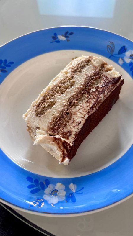 Кусок тирамису на синей тарелке: слоистый десерт с кремом и посыпкой, крупный план десерта в кафе «Лолита» в Москве.