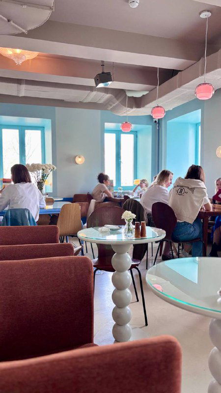 Общий вид зала «Лолиты»: посетители за столиками, большие окна с голубыми рамами, мягкие диваны и светлая уютная обстановка.