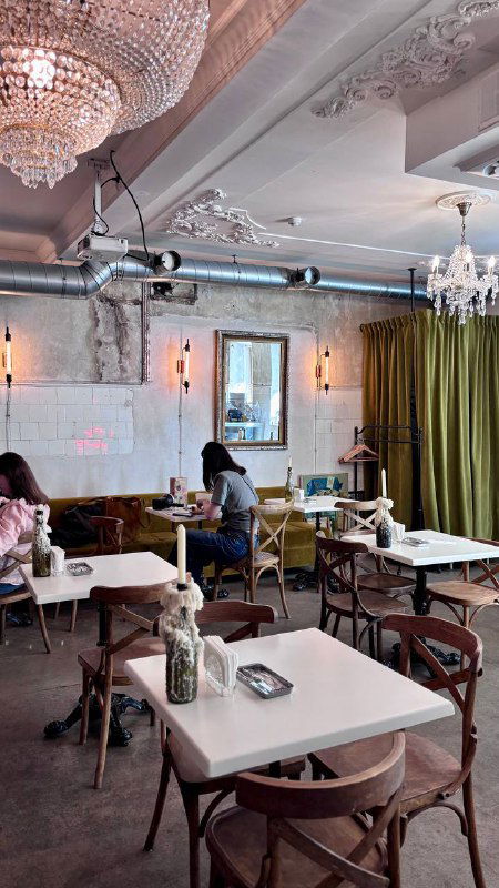 Интерьер зала кафе с люстрами, столиками и шторами; стильное пространство, где иногда проходят киновечера и показы в оригинале.