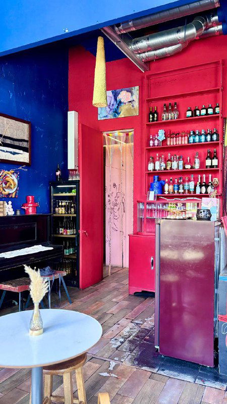 Интерьер с красными и синими акцентами, открытый проход к кухне и небольшие столики — сочетание художественного пространства и уютного кафе в Москве.