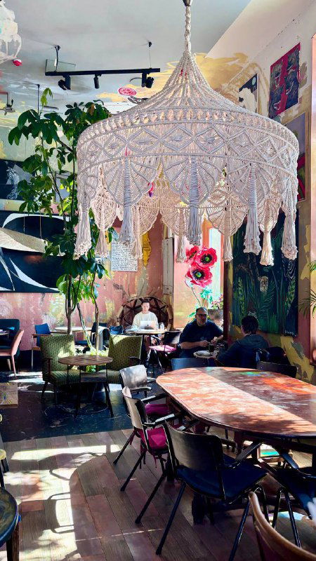 Крупный макраме-абажур над обеденной зоной, мягкие кресла и столы, декоративные растения и свет — художественный интерьер кафе-галереи в Москве.