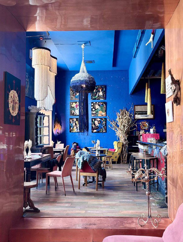 Общий вид зала с высокими потолками, синими стенами, витражами и картинами — сочетание художественного пространства и уютного кафе в центре Москвы.