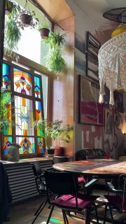 Столики у витражного окна с макраме-абажуром, солнечный свет и растения создают живую, уютную атмосферу ресторана-галереи «Узоры» в Москве.