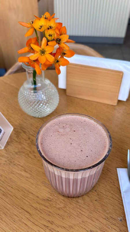 Какао или шоколадный напиток в стеклянном стакане на столе с небольшой вазой цветов и салфетницей — атмосферный кадр из интерьера Nobo.