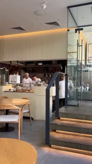 Интерьер кафе Nobo: открытая кухня, повара за барной стойкой, ступеньки и современный минималистичный дизайн в обеденное время.