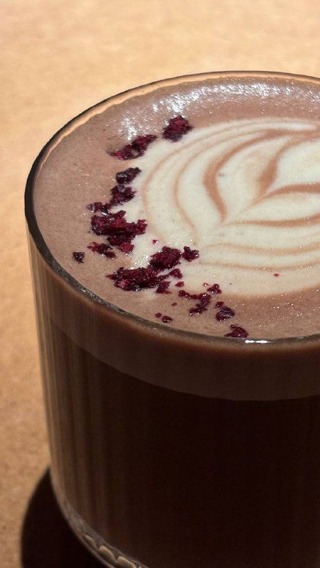 Стакан spicy rum какао с латте-арт и крошками ягод на поверхности, тёплый напиток в стеклянной посуде на столе ресторана.