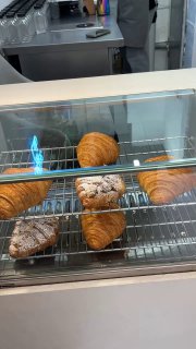 Витрина с несколькими круассанами и выпечкой на металлических решетках под подсветкой — свежая выпечка за стеклом