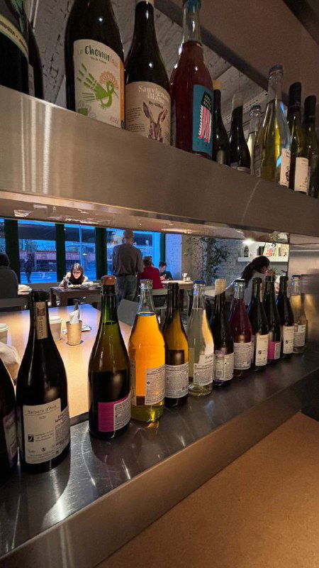 Ряд бутылок и натуральных вин на барной стойке ресторана, отражение в стекле и вид интерьера винного бара вечером.