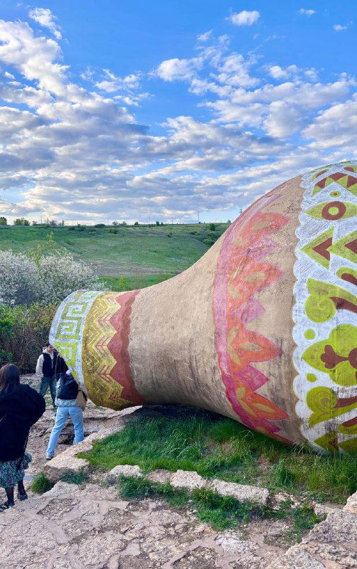 Большая разрисованная керамическая амфора на склоне как арт-объект, посетители спускаются рядом по тропе.