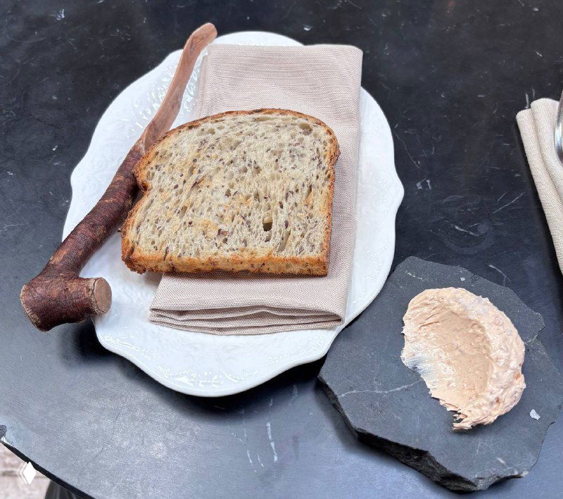 Поджаренный цельнозерновой хлеб и собственноручно приготовленное масло, подача на тарелке и каменной разделочной пластине, крупный план.