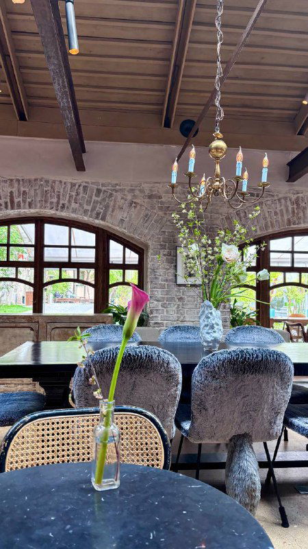 Столовая зона с хрустальной люстрой и арочными окнами, столики у окна с вазочками и винтажным декором под деревянным потолком.